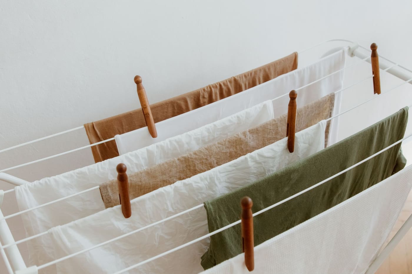 Light-colored garments hanging on a white folding drying rack with wooden pegs