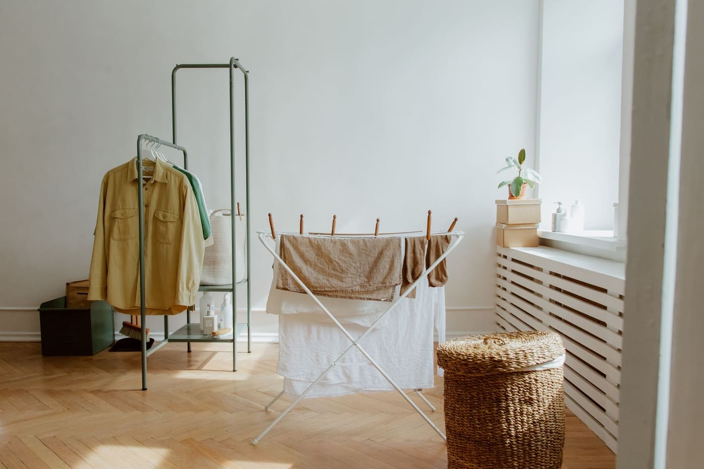 A bright room with a folding drying rack holding clothes beside a clothes rail