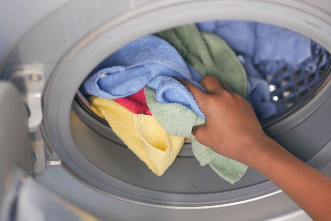 A hand loading colorful towels into a front-loading washing machine