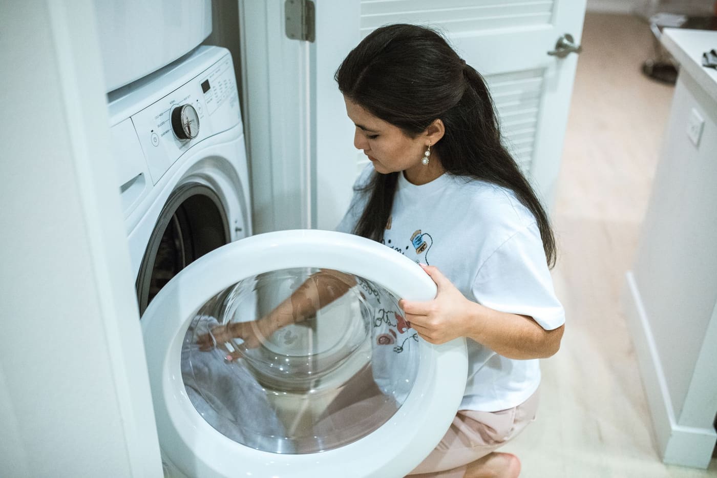 A woman kneeling to open the door of a front-loading washing machine