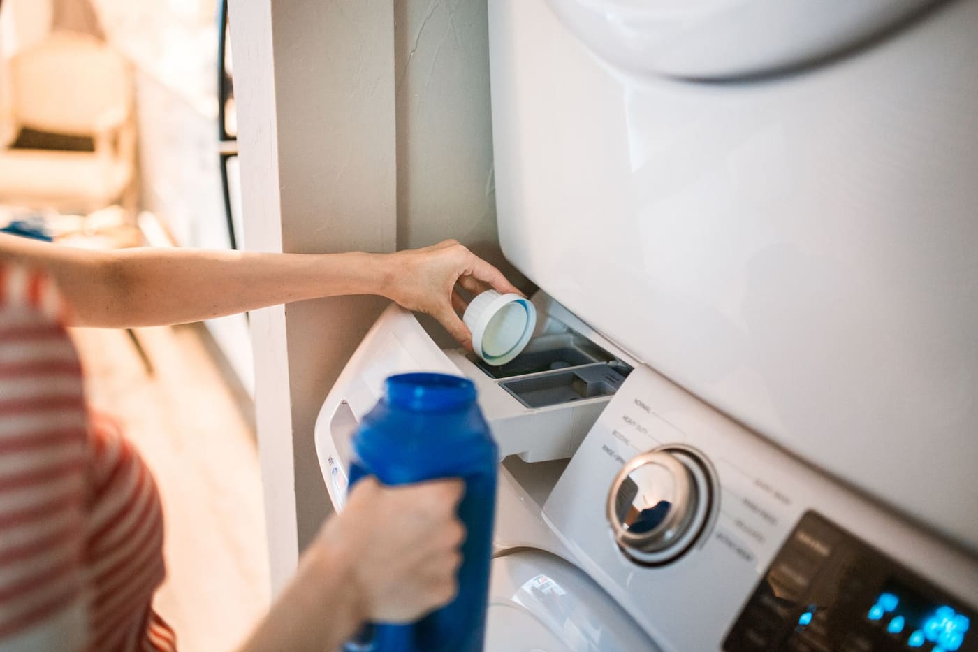A person pouring liquid detergent into the drawer of a front-loading washer
