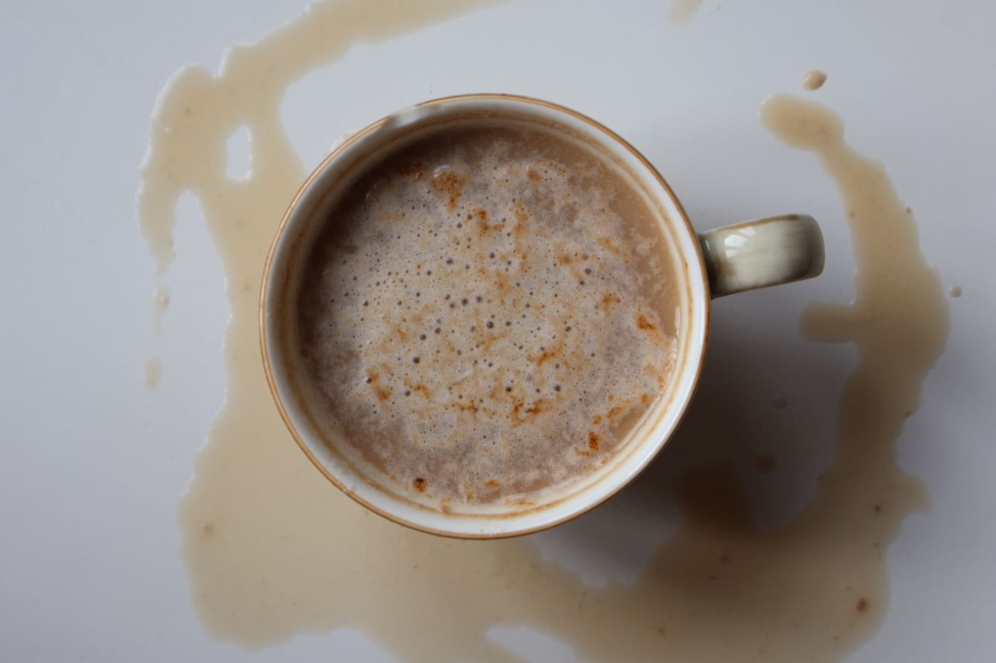 A cup of coffee seen from above with a spill spreading across a white surface
