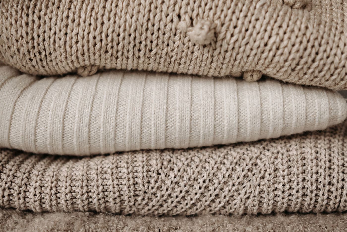 Close-up of a stack of beige and cream knit sweaters showing different knit textures